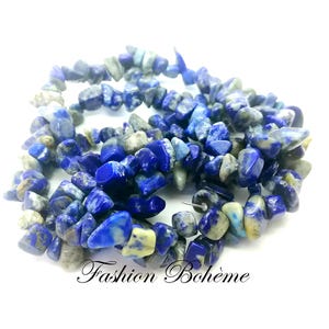 Könnte beinhalten: Eine Strähne aus blauen und weißen Lapislazuli-Chips. Die Perlen sind unregelmäßig in Form und Größe und haben eine natürliche, raue Textur.