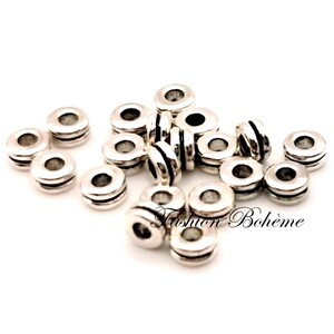 May include: A collection of silver-colored spacer beads. Each bead is cylindrical with a central hole and two grooved bands. The text "Fashion Boh&egrave;me" is visible in the lower right corner.