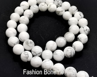May include: A strand of white howlite beads, each bead is round and has a marbled pattern. The beads are strung on a clear elastic cord.