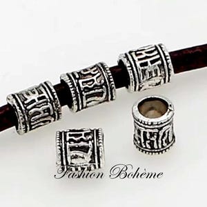 Könnte beinhalten: Silberne Metallperlen mit einem gravierten Design. Die Perlen sind auf einer braunen Lederkordel aufgereiht.