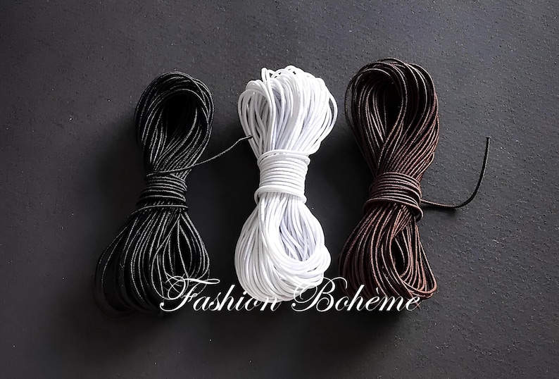 May include: Three bundles of cord in black, white, and brown against a dark background. The cords are tightly wound and appear to be made of a smooth, flexible material. The text "Fashion Boh&egrave;me" is visible.