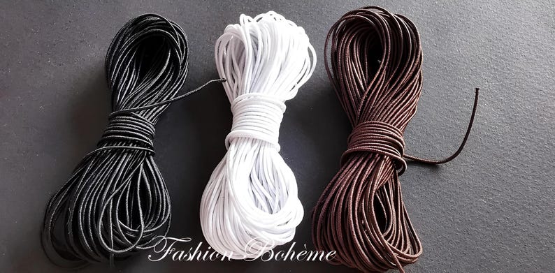 May include: Three spools of cord in black, white, and brown. The cords are tightly wound, with loose ends visible. The image is set against a dark background. The text "Fashion Boh&egrave;me" is in the bottom center.