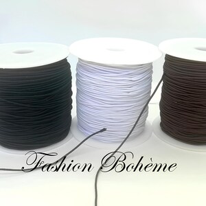 May include: Three spools of elastic cord in black, white, and brown. The spools are on white cardboard bases. The text "Fashion Boh&egrave;me" is at the bottom of the image.