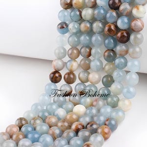 Peut inclure: Un brin de perles rondes en pierres précieuses bleues et brunes. Les perles ont un aspect marbré et moucheté.