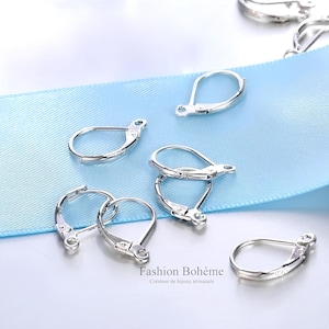 Peut inclure: Crochets d'oreilles argentés, également appelés fermoirs à levier, sont présentés sur un ruban bleu clair. Les crochets sont conçus pour être utilisés avec des boucles d'oreilles ayant une boucle ou un anneau de jonction.