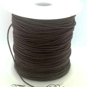 May include: A spool of dark brown elastic cord. The cord is tightly wound around a white plastic spool. The text "Fashion Boh&egrave;me" is written in cursive at the bottom of the image.