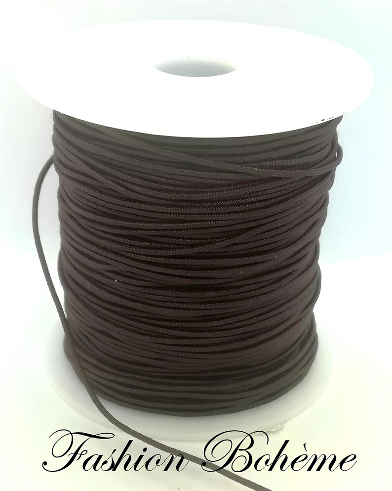May include: A spool of dark brown elastic cord. The cord is tightly wound around a white plastic spool. The text "Fashion Boh&egrave;me" is written in cursive at the bottom of the image.