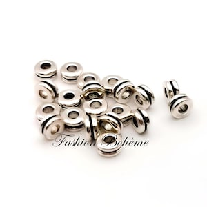 May include: A collection of silver-colored metal beads with a cylindrical shape and a central hole. The beads have a grooved design around the middle. The text "Fashion Boh&egrave;me" is visible on the bottom of the image.