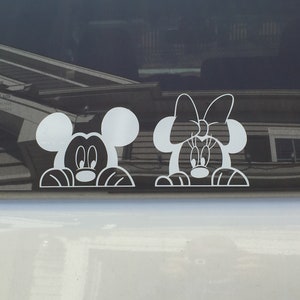 Puede incluir: Pegatinas de vinilo blanco de Mickey Mouse y Minnie Mouse asomándose por encima de una superficie. Mickey Mouse tiene orejas grandes y una nariz negra. Minnie Mouse tiene un gran lazo en la cabeza y una nariz negra.