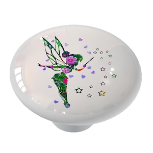 May include: A white ceramic knob with a colorful floral fairy design. The fairy is holding a wand and surrounded by stars and hearts.