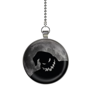 May include: A silver chain with a round pendant featuring a black silhouette of the character Oogie Boogie from the movie The Nightmare Before Christmas against a gray moon background.