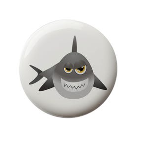 May include: A white button with a cartoon gray shark with yellow eyes and a toothy grin. The shark is facing forward with its mouth open.