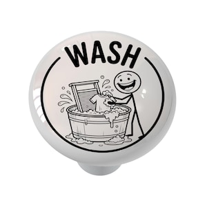 May include: White ceramic cabinet knob with a black and white illustration of a stick figure washing clothes in a tub. The word "WASH" is printed in black on the knob.