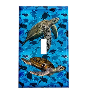 May include: A light switch cover featuring a blue background with a pattern of sea turtles. Two sea turtles are in the foreground, one is green and the other is brown.