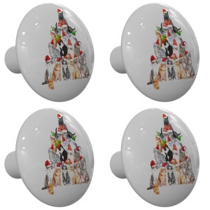 May include: Set of four white ceramic cabinet knobs with a Christmas tree design featuring cats wearing Santa hats. The cats are arranged in a pyramid shape, with the largest cat at the top and the smallest cats at the bottom.