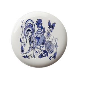 May include: A white ceramic plate with a blue and white rooster design. The rooster is surrounded by blue and white flowers and leaves.