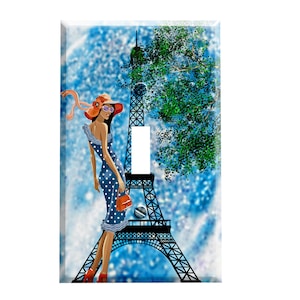 May include: A light switch cover featuring a woman in a blue polka dot dress and a red hat standing in front of the Eiffel Tower. The background is a blue and white watercolor effect.