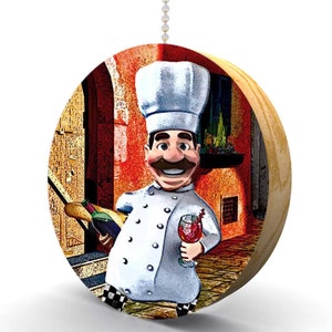 May include: A round wooden pull chain with a colorful image of a cartoon chef holding a bottle of wine and a glass of red wine. The chef is wearing a white chef's hat and a white chef's coat with black buttons. The background is a colorful Italian street scene.