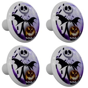 May include: Four white ceramic cabinet knobs with a purple and white background featuring a black and white illustration of Jack Skellington from The Nightmare Before Christmas holding a jack-o-lantern.