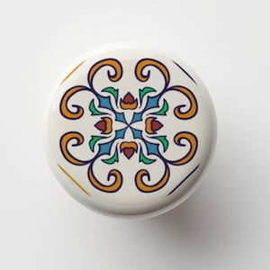 May include: A white ceramic knob with a colorful floral design. The design features blue, green, orange, and red colors. The knob is round and has a smooth surface.