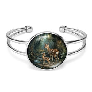 May include: Silver bangle bracelet with a round glass cabochon featuring a painting of two deer in a forest setting.