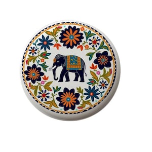 May include: A round, white decorative plate featuring a blue elephant with a patterned blanket. The plate is adorned with a floral border in shades of blue, orange, and green. The design has an Indian aesthetic.