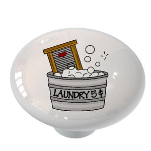 May include: A white ceramic knob with a cartoon illustration of a laundry basket with soap suds and a clothes wringer. The text "LAUNDRY 5$" is on the basket.