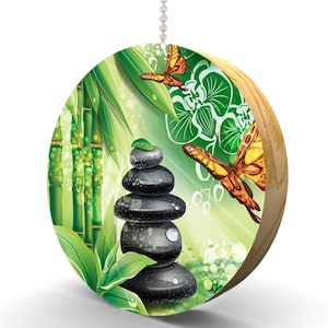 May include: A round wooden ornament with a green, yellow, and black design. The design features a stack of black stones, bamboo stalks, green leaves, and two yellow butterflies.