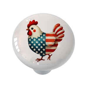 May include: A white ceramic cabinet knob featuring a watercolor illustration of a rooster. The rooster's body is split, with the left side displaying a blue field of white stars and the right side showing red and white stripes, resembling the American flag.