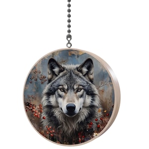 May include: A round wooden ceiling fan pull featuring a detailed illustration of a wolf's face. The wolf has gray and black fur, with amber eyes and a black nose. The background has a blue and brown color scheme with red berries.