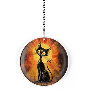 May include: Round, decorative hanging ornament featuring a stylized black cat with yellow eyes and whiskers. The cat is set against a warm, sunset-like background with a white border. A silver chain is attached for hanging.