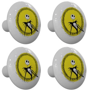 May include: Set of four ceramic cabinet knobs featuring a black and white illustration of Jack Skellington from The Nightmare Before Christmas. The illustration shows Jack Skellington standing in front of a yellow sun with a black outline.