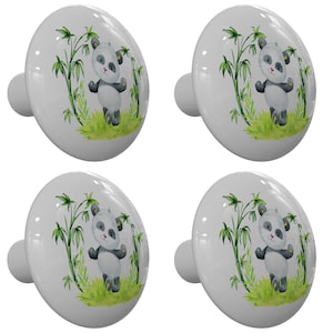 May include: Four white ceramic cabinet knobs with a panda bear design. Each knob features a panda standing in green grass with bamboo stalks. The panda is black and white with gray accents. The knobs have a rounded shape and a silver-colored stem.