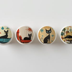 May include: Set of four ceramic knobs featuring black cats in various mid-century modern settings. The knobs are round and have a white background.