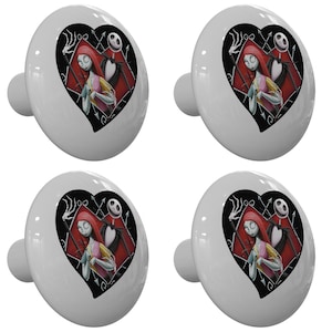 May include: Four white ceramic cabinet knobs with a black heart-shaped design featuring a cartoon image of Jack Skellington and Sally from the Nightmare Before Christmas movie. The heart design has a red background with black outlines.