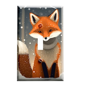 May include: A light switch cover featuring a cute cartoon fox wearing a white scarf and sitting in the snow. The fox has orange fur, a white chest, and black eyes. The background is a snowy forest scene.