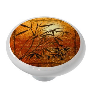 May include: A ceramic knob with a design of black bamboo silhouettes against a gold and orange background.