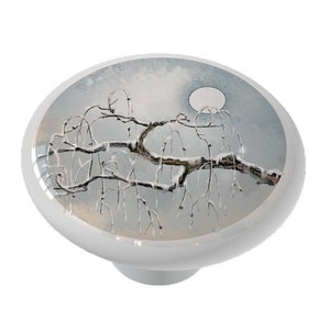 May include: A ceramic knob with a wintery scene of a snow-covered tree branch with a full moon in the background.