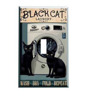 May include: A light switch cover featuring a vintage-style illustration of a washing machine with two black cats. The text "BLACK CAT LAUNDRY" is above the washing machine and "WASH - DRY - FOLD - REPEAT" is below.