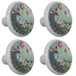 May include: Four ceramic cabinet knobs with a teal background featuring a peacock with a spread tail and red lanterns. The peacock is surrounded by pink flowers and green leaves.