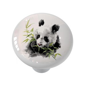 May include: White ceramic cabinet knob featuring a watercolor panda bear design. The panda is depicted in black and white, eating bamboo leaves. The knob has a glossy finish and a silver-colored base.