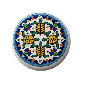May include: A white ceramic plate with a blue, yellow, green, and orange design of four turtles in a circular pattern.