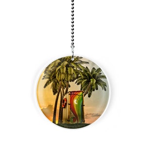 May include: A round, white ceramic fan pull with a colorful image of a outhouse with a rainbow door and palm trees in the background.