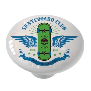 May include: A white ceramic knob with a green skateboard with a skull design and blue wings. The text "Skateboard Club" is written in a circle around the skateboard. The text "Young Wild and Free" is written on a banner below the skateboard. The text "Estd 1986" is written above the skateboard.