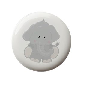 May include: A round, white button with a cartoon elephant illustration. The elephant is gray with large ears, a curled trunk, and pink cheeks. The button is a cute accessory.