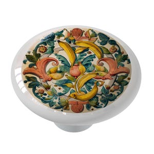 May include: A ceramic knob with a colorful floral design featuring yellow bananas, red flowers, and green leaves. The design is reminiscent of a vintage Italian majolica tile.