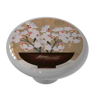 May include: A ceramic knob with a floral design. The knob features a brown pot with white flowers and a light brown background.
