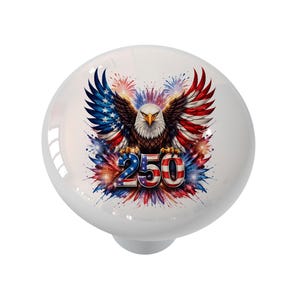 May include: White ceramic cabinet knob featuring a patriotic design. The knob showcases a detailed illustration of an American bald eagle with outstretched wings, colored in red, white, and blue. The number "250" is prominently displayed below the eagle.