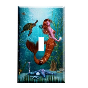 May include: A light switch cover featuring a mermaid with orange and brown scales, red hair, and a pearl in her hand. The mermaid is swimming in a blue ocean with a sea turtle, seaweed, and bubbles.
