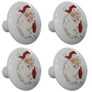 May include: Set of four white ceramic cabinet knobs with a vintage illustration of Santa Claus wearing a red hat and white beard. The knobs are round and have a small stem on the back for attaching to a cabinet door.